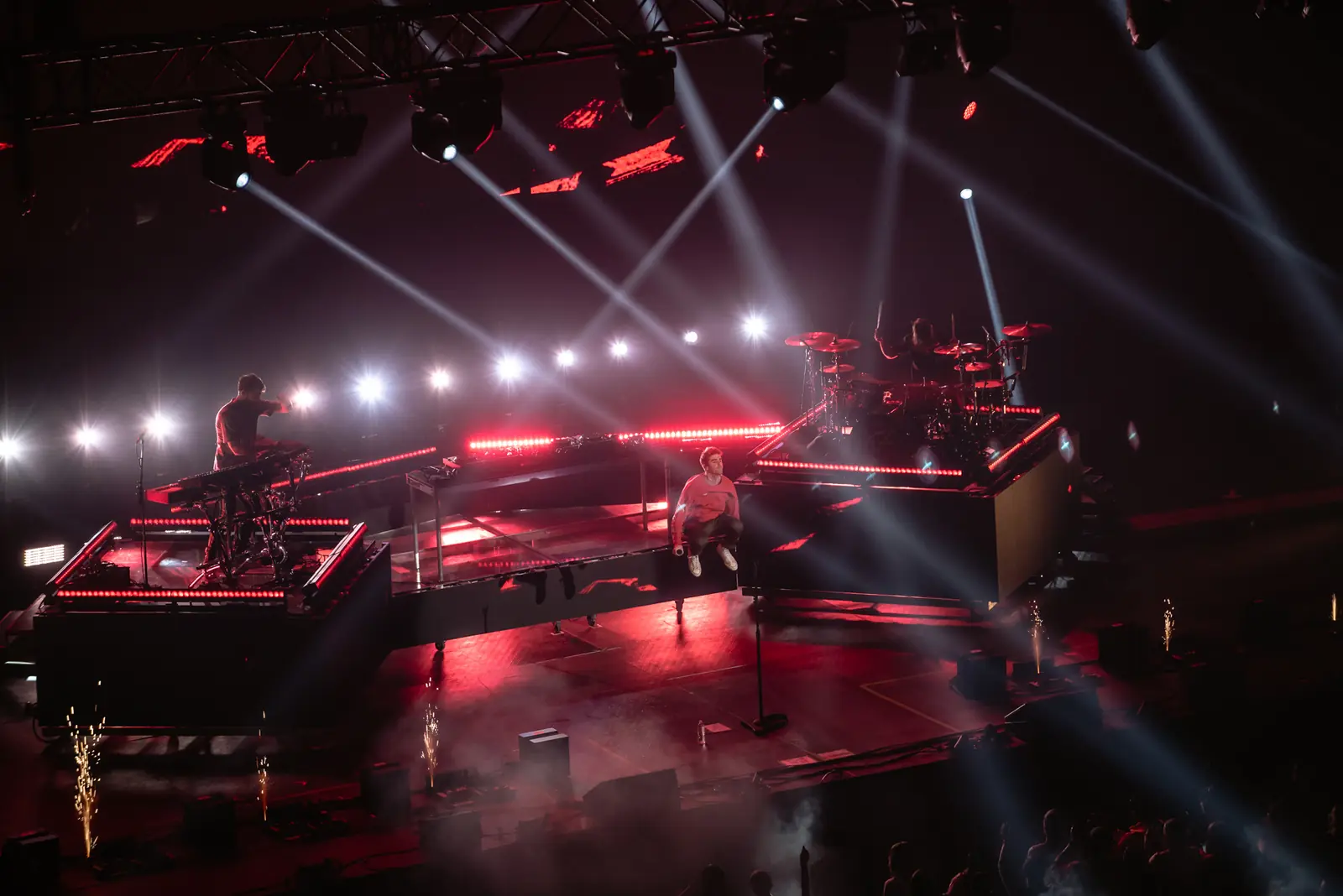 Stage washed in red light with beams from overhead truss