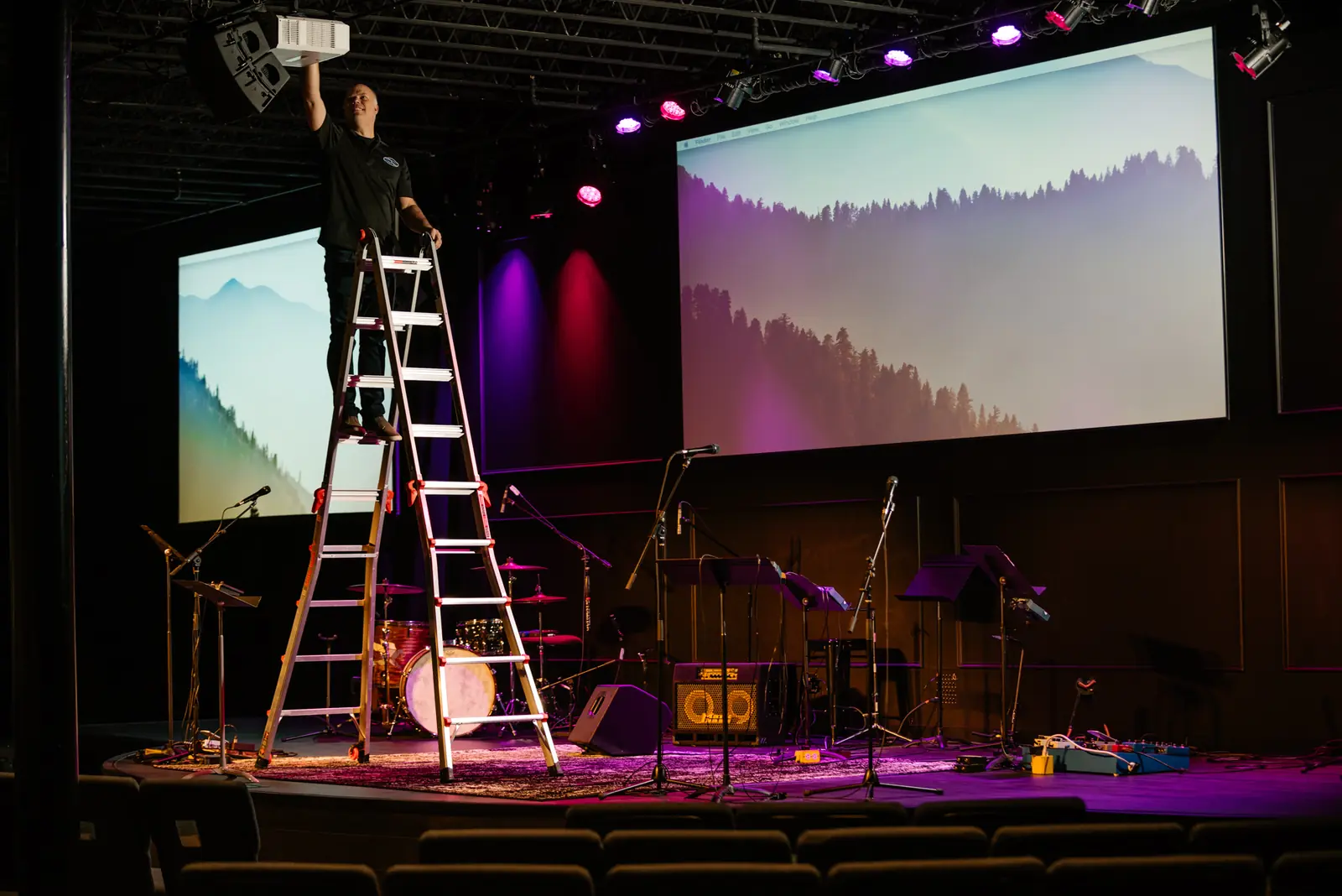 Installer adjusting a fixture above a church stage with projection screens